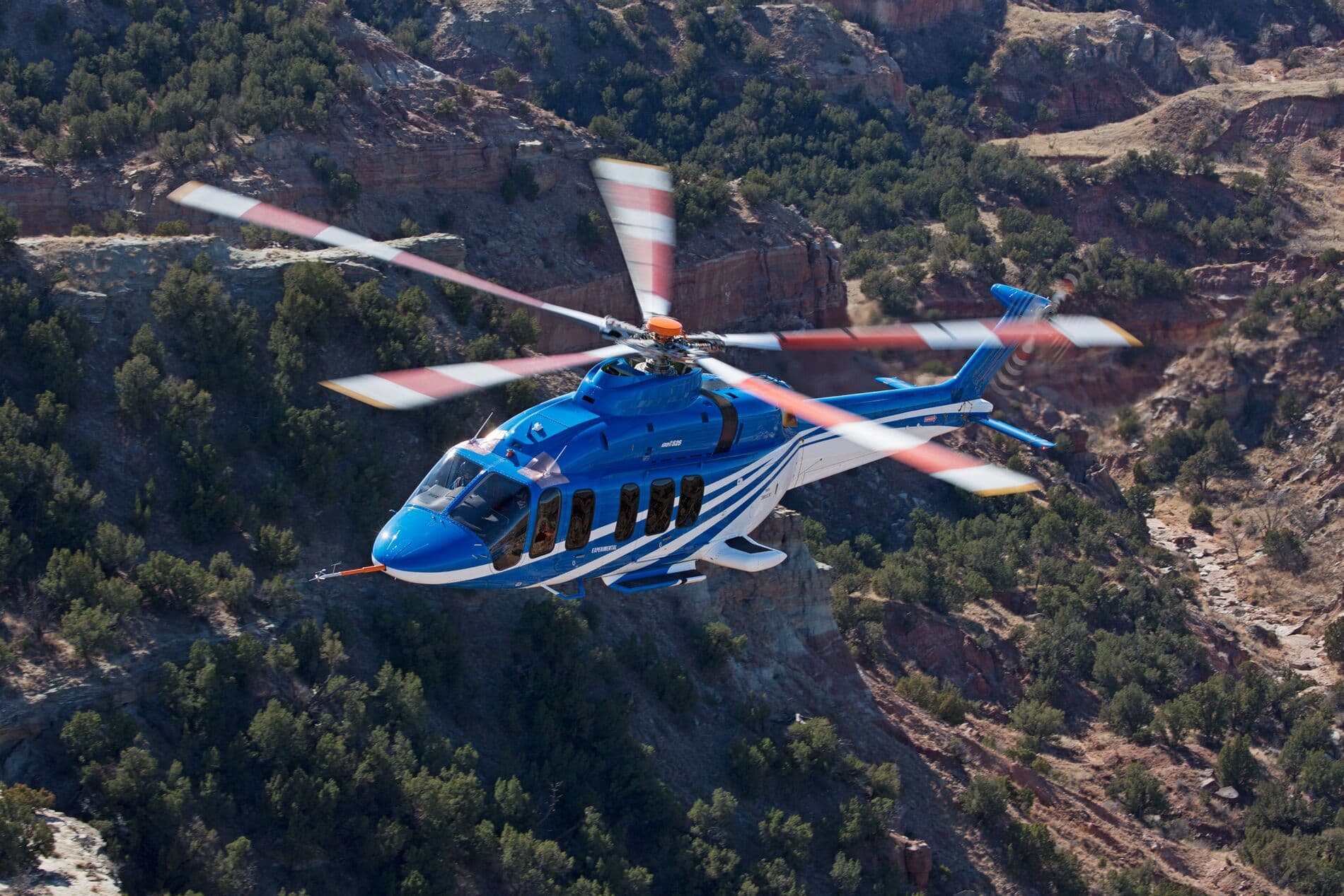 Bell 525 im Flug über grünen Bergen in der Wüste